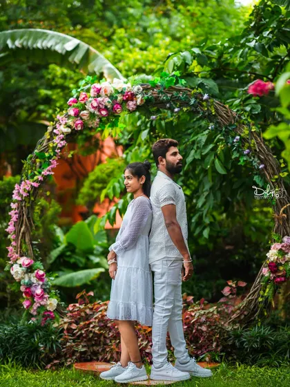 A couple stands back-to-back in front of a rustic floral arch, a creative and stylish pose.