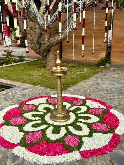 A beautiful flower rangoli (pookalam) with a traditional brass lamp at its center, a classic element for welcoming guests to a South Indian event.