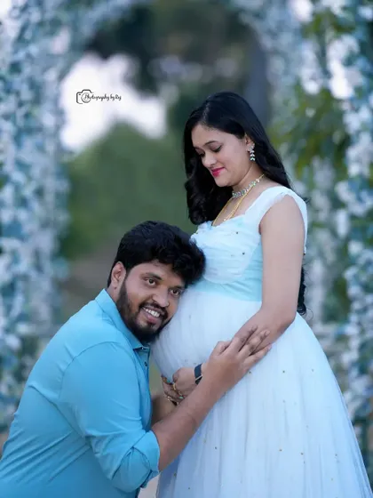 A heartwarming pose where the father-to-be listens to the baby bump. This shot, taken under our white floral arch, is a favorite for capturing the couple's connection.