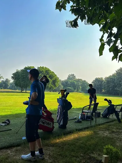 A quiet moment of focus on the range. A golfer prepares for a shot, with golf bags ready for a full session of practice.