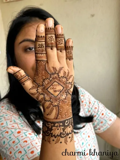 A simple and meaningful back of hand design. This mehendi features the wedding date inside a diamond-shaped frame, surrounded by floral patterns and auspicious symbols on the fingers.
