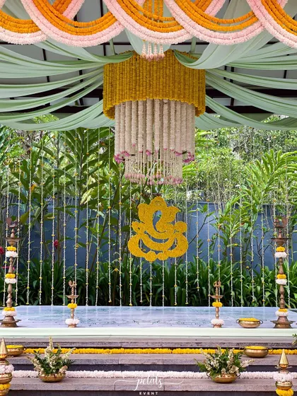 A beautiful and intricate setup for a traditional ceremony, with a floral chandelier, a Ganesha motif, and traditional props.