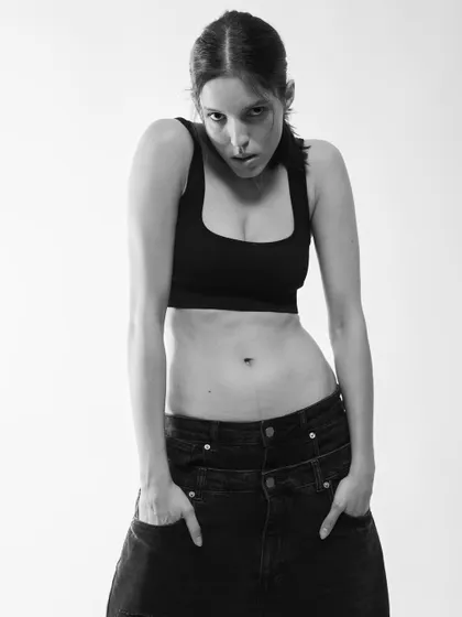 A raw, simple black and white portrait. The focus is on the model's direct gaze and strong presence.