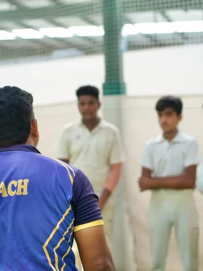A coach addresses a group of young players in the nets. These moments of direct feedback, whether advice or a stern talk, are crucial for development.