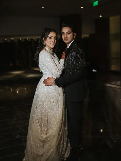 A classic couple portrait from the Sangeet ceremony. The bride's shimmering white lehenga and soft glam makeup look absolutely stunning next to her partner's sharp tuxedo.