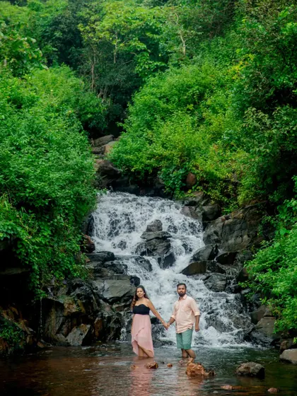 A beautiful wide-angle shot of the couple standing in the water before a lush, green waterfall. This showcases the epic scenery we can incorporate into your pre-wedding session.