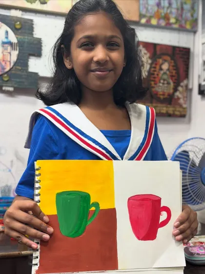Look at that proud smile. One of our youngest artists shows off her work from a foundational drawing class where she learned about color, shape, and composition by painting simple objects like mugs.