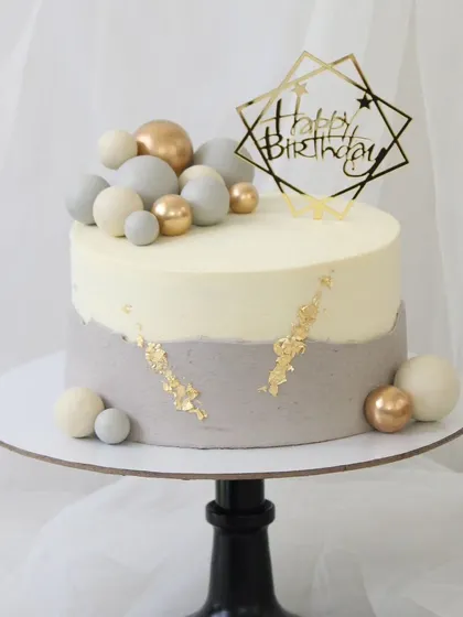 A serene and modern birthday cake with a two-tone grey and white design. This minimalist cake is accented with a touch of gold leaf and a cluster of matching spheres.