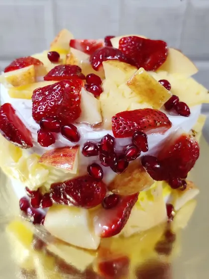 A mini fresh fruit cake, perfect for a small celebration. It's generously topped with a mix of chopped fruits.