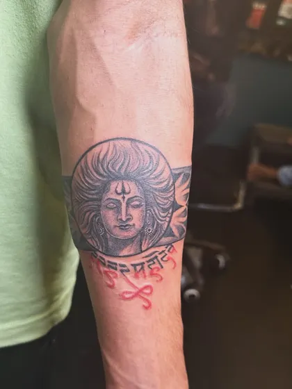 A different angle of the Shiva armband tattoo, showing the intricate details of his hair and the tribal patterns on the band. The combination of portrait and pattern work makes it unique.