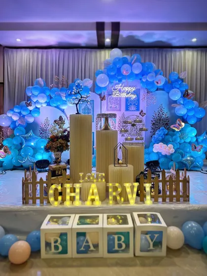 A beautiful baby blue themed birthday stage. The setup includes a custom backdrop, multiple balloon arrangements, 'BABY' blocks, and marquee letters, all in a cohesive blue and white color scheme.