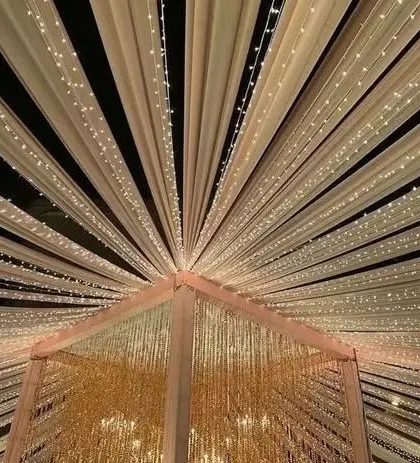 A beautiful ceiling treatment with drapes and fairy lights radiating from the center. This design adds a touch of glamour and grandeur to any indoor or tented venue.