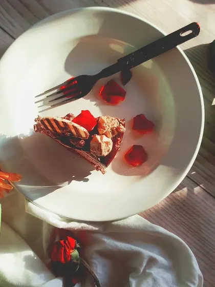 A top-down shot of the last bite of chocolate pastry on a plate, surrounded by flowers. This flatlay tells the story of a delicious dessert enjoyed, leaving you wanting more.