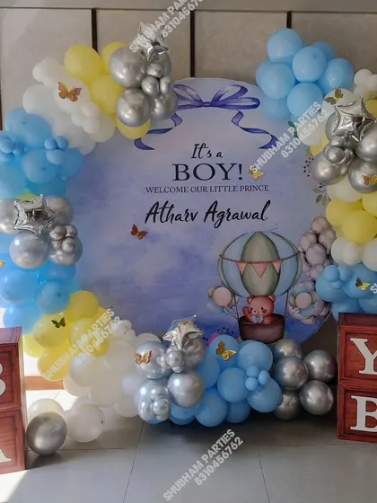Announce the arrival of your little prince with this adorable "It's a Boy!" baby announcement decoration. The setup features a custom circular backdrop with a hot air balloon theme, surrounded by a balloon arch in shades of blue, yellow, and silver.
