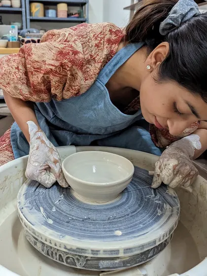 A student carefully removes her freshly thrown bowl from the wheel, a moment of accomplishment.