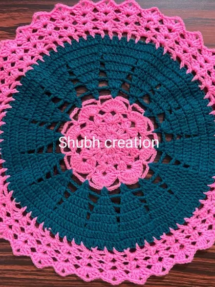 This round crochet mat features a striking color combination of deep teal and bright pink in a geometric pattern.