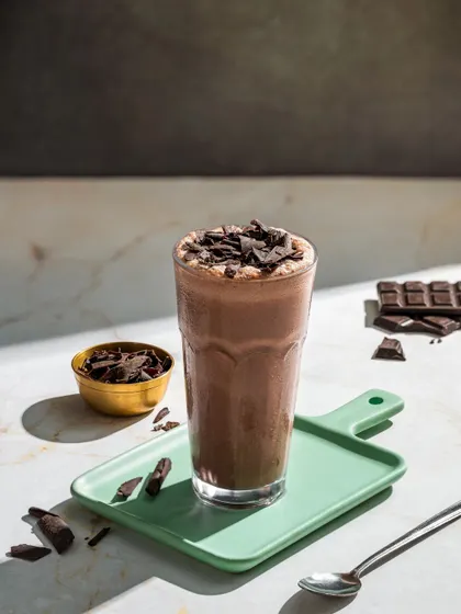 A rich dark chocolate milkshake, topped with chocolate shavings and styled with pieces of a chocolate bar.