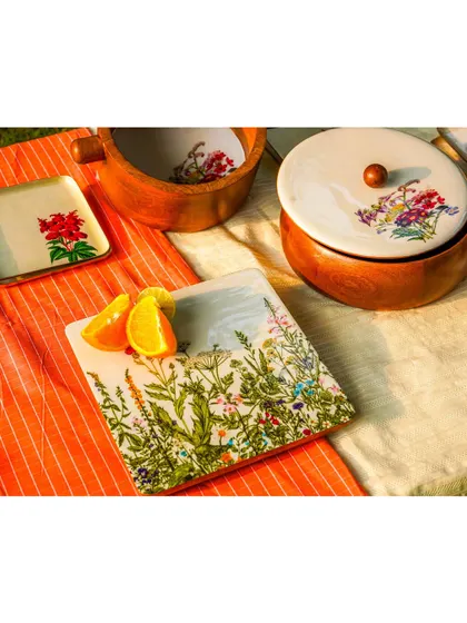 An outdoor 'golden hour' shot of a tablescape with wooden bowls and floral-painted plates. The warm, natural light gives the products a beautiful glow.