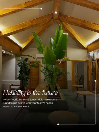 A breakout zone designed for flexibility, featuring a high ceiling with exposed wooden beams and large plants. This space supports hybrid work models with multi-use furniture for casual meetings or quiet relaxation.