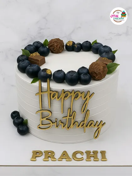 This cake shows our love for elegant and minimalist designs. A clean, white buttercream finish is topped with fresh blueberries, chocolate truffles, and a personalized gold acrylic nameplate for a sophisticated birthday celebration.