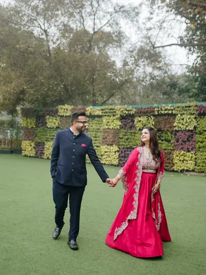 A happy couple walks hand-in-hand across a lush green lawn during their Roka ceremony, sharing a look of love.