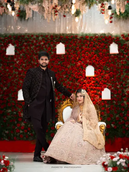 Another angle of the couple against the red rose backdrop, showcasing their beautiful traditional attire.