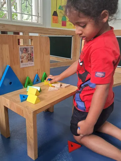 This child explores geometric shapes by arranging colorful magnetic tiles on a wooden chair. This play-based math activity encourages pattern recognition and creativity.