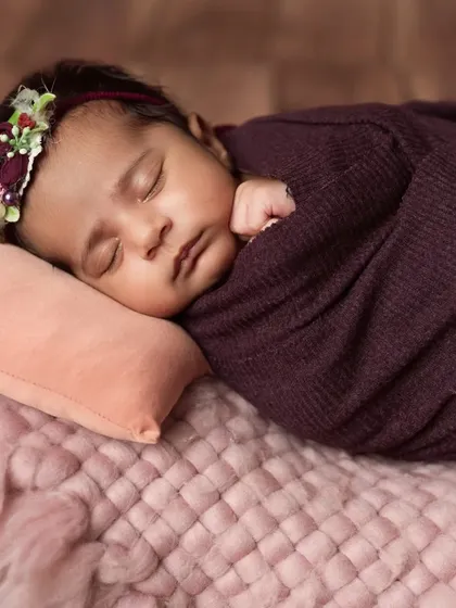 A close-up on the face of the sleeping baby girl in her purple wrap and floral headband.