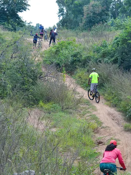 A group cycling down a dirt path in Ramanagara, surrounded by lush greenery.