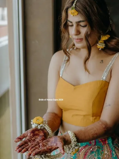A quiet moment of admiration. The bride looks at her beautifully stained hands, adorned with floral jewelry, during what looks like her haldi or mehendi ceremony.