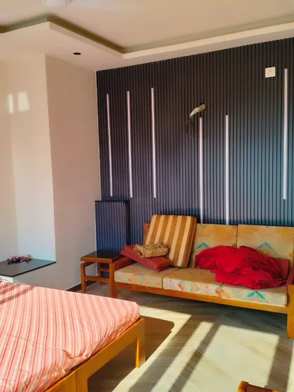 The interior of the Palam Vihar terrace room, featuring a bed and sofa against a modern, vertically paneled accent wall.