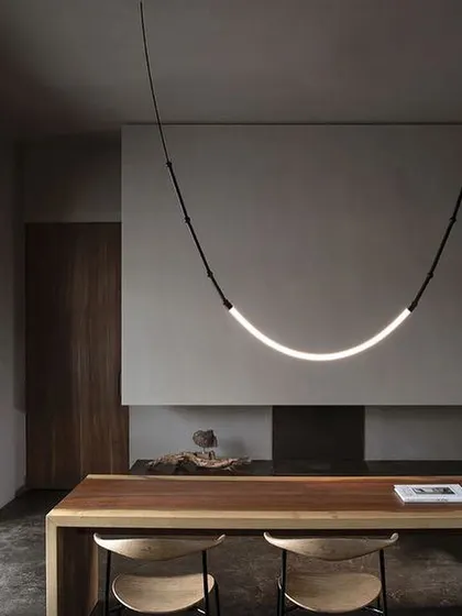 A single, graceful arc of the Leda light over a wooden table. This minimalist configuration highlights the fixture's elegant simplicity and warm, diffused illumination.