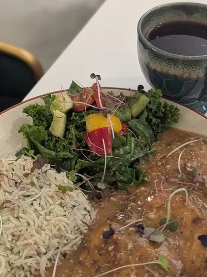 A healthy and visually appealing meal of grilled chicken in sauce, rice, and a fresh salad, paired with black coffee. Eating out can be healthy if you make smart choices.