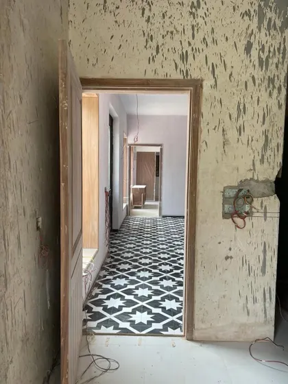 A work-in-progress shot from a renovation, showing the raw beauty of a space being reborn. The newly laid patterned tiles are a hint of the character to come, seen through a doorway in a wall that is still waiting for its final touch.
