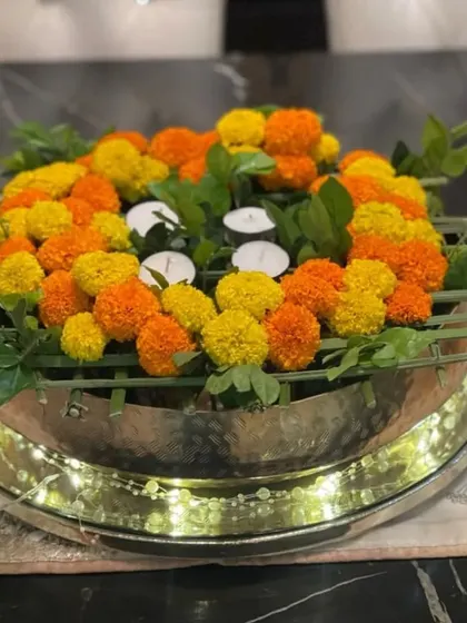 This floral centerpiece in a silver urli is designed to transform moments into memories. The arrangement of marigolds and tea lights, surrounded by fairy lights, creates an ambiance of serenity and joy.