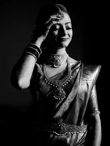 A dramatic, low-key black and white portrait of the bride, highlighting the texture of her saree and jewelry.
