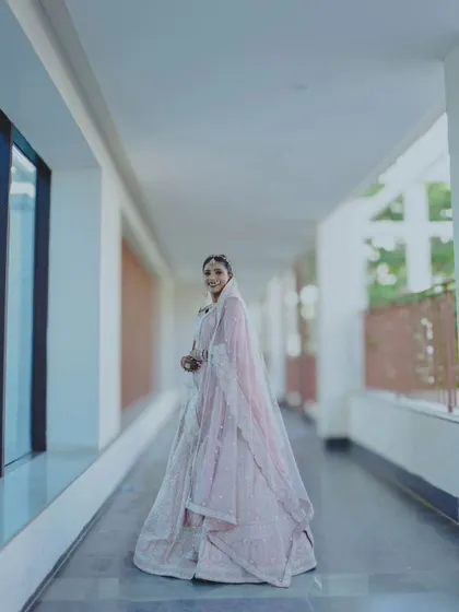 A full-length shot of the bride in a corridor, showcasing the beautiful drape and flow of her wedding lehenga.