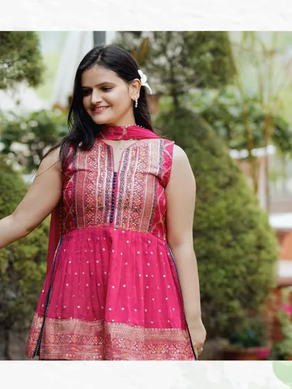 A lovely portrait of a woman in a pink and gold outfit, smiling in a lush garden setting. The natural light and greenery make for a fresh and vibrant photo.