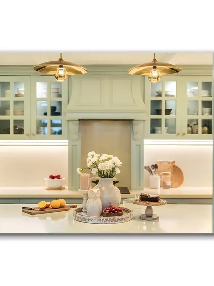 A view into the powder blue kitchen, framed by a doorway. The soft lighting and elegant details, like the custom range hood and glass-fronted cabinets, are perfectly captured, showcasing a dream kitchen.