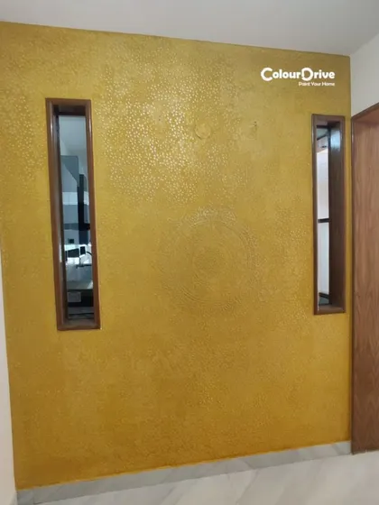 A completed Calcecruda texture design in a vibrant yellow, applied to a pooja room entryway. The intricate stencil work within the texture adds a traditional yet modern touch to the space.