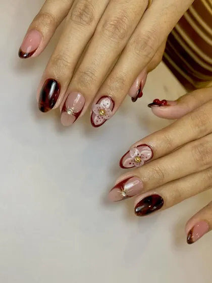A rich and detailed design combining a tortoise shell pattern, deep red French tips, and a beautiful 3D flower with a gold bead center.