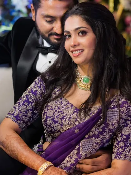 The lovely Vidya Dhare sharing a happy moment at her reception. Her makeup features a soft, romantic feel with a focus on glowing skin and a gentle smile, perfect for her embroidered purple lehenga.