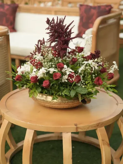 A lush floral centerpiece in a brass bowl, featuring a mix of red and white flowers, placed on a modern wooden table at the wedding reception.
