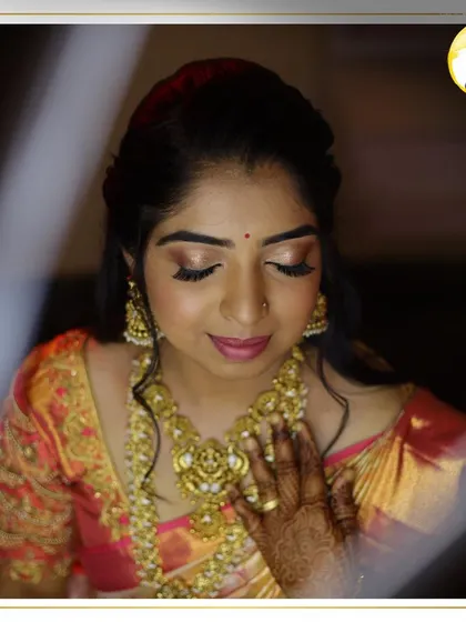 A candid moment of bridal beauty. This look features a soft, golden shimmer on the eyes and a warm pink lip, perfectly complementing the bride's intricate gold jewelry and peach-toned Kanjeevaram saree.