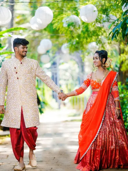 A happy walking shot of a couple in traditional wear, hand-in-hand down a garden path.