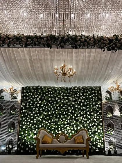 A detailed shot of the magnificent Nikaah or Walima stage. The design features a dense wall of white flowers, framed by elegant white drapes and beautiful chandeliers.