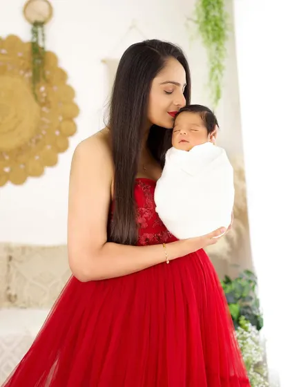 A close-up of a mother in a red gown, gently kissing her newborn's head. This is a tender and emotional moment between mother and child.