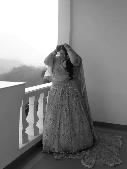 A candid black and white photo of the bride adjusting her hair on the balcony, a natural and unposed moment of preparation.