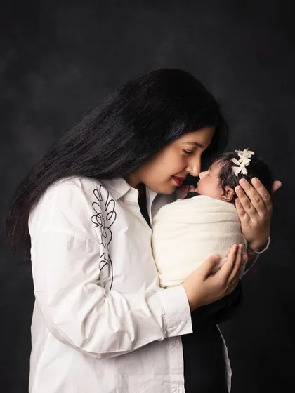 An intimate mother and child portrait against a dark, classic backdrop. The simplicity of the setting emphasizes the tender connection and the baby's delicate features.