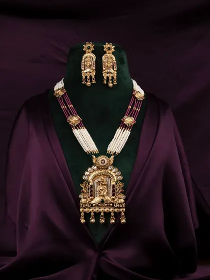 An opulent traditional Indian necklace and earring set, professionally displayed on a bust against a rich, dark purple satin background to highlight the intricate gold work and gemstones.